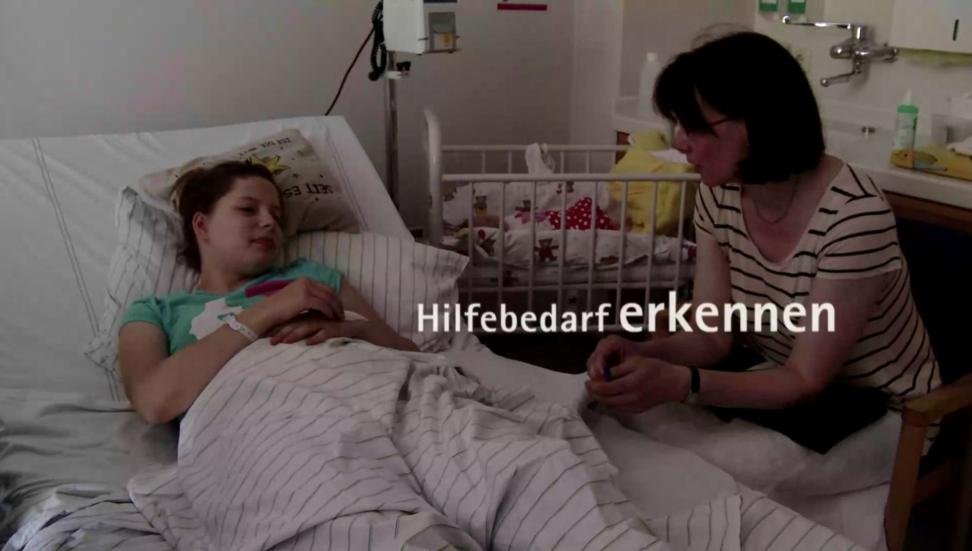 Videostill mit dem Schriftzug „Hilfebedarf erkennen“, eine Frau im Krankenbett im Gespräch