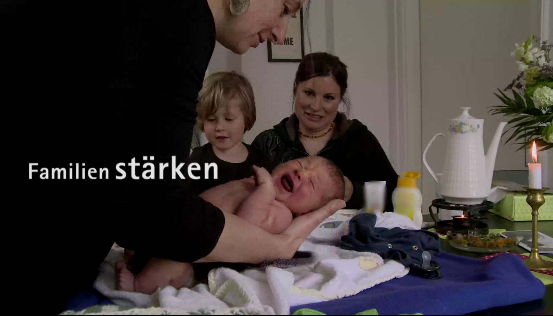 Videostill mit dem Schriftzug „Familien stärken“, eine Frau hält ein schreiendes Neugeborenes