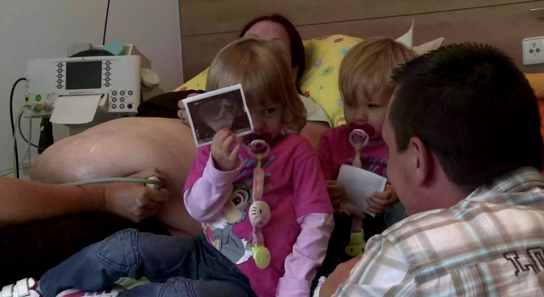 Videostill: Ultraschallbild einer Schwangerschaft, zwei Kinder betrachten es mit den Eltern