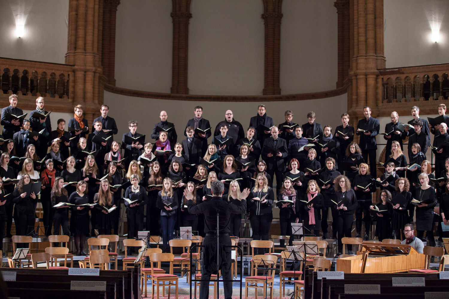 Chor und Orchester musizieren in einer Kirche, der Dirigent von hinten zu sehen
