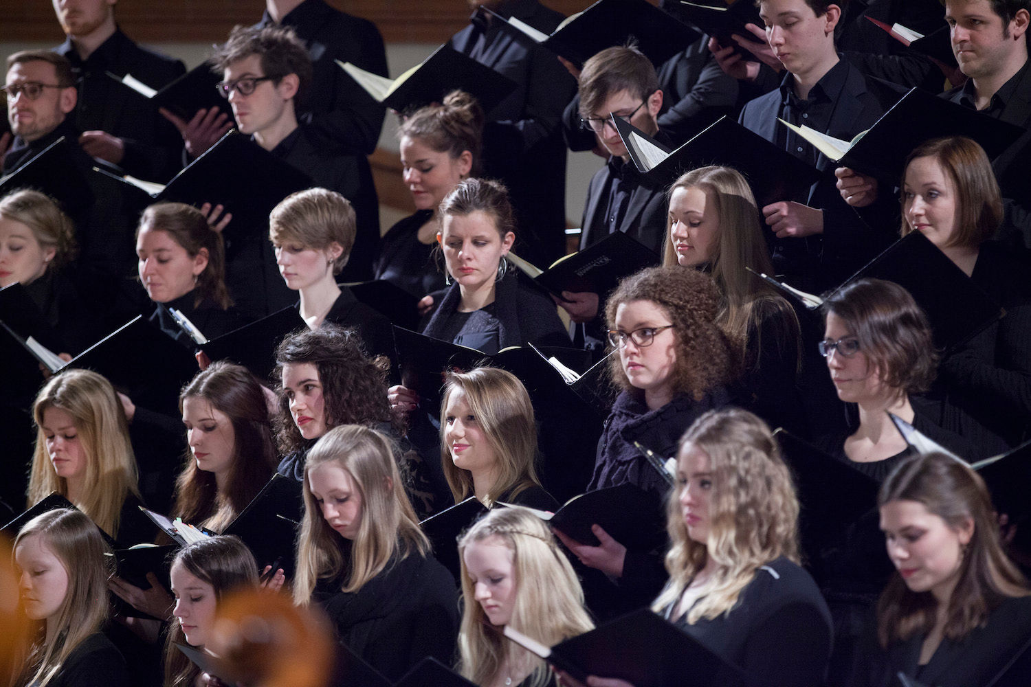 Chormitglieder mit Notenmappen singen konzentriert in mehreren Reihen