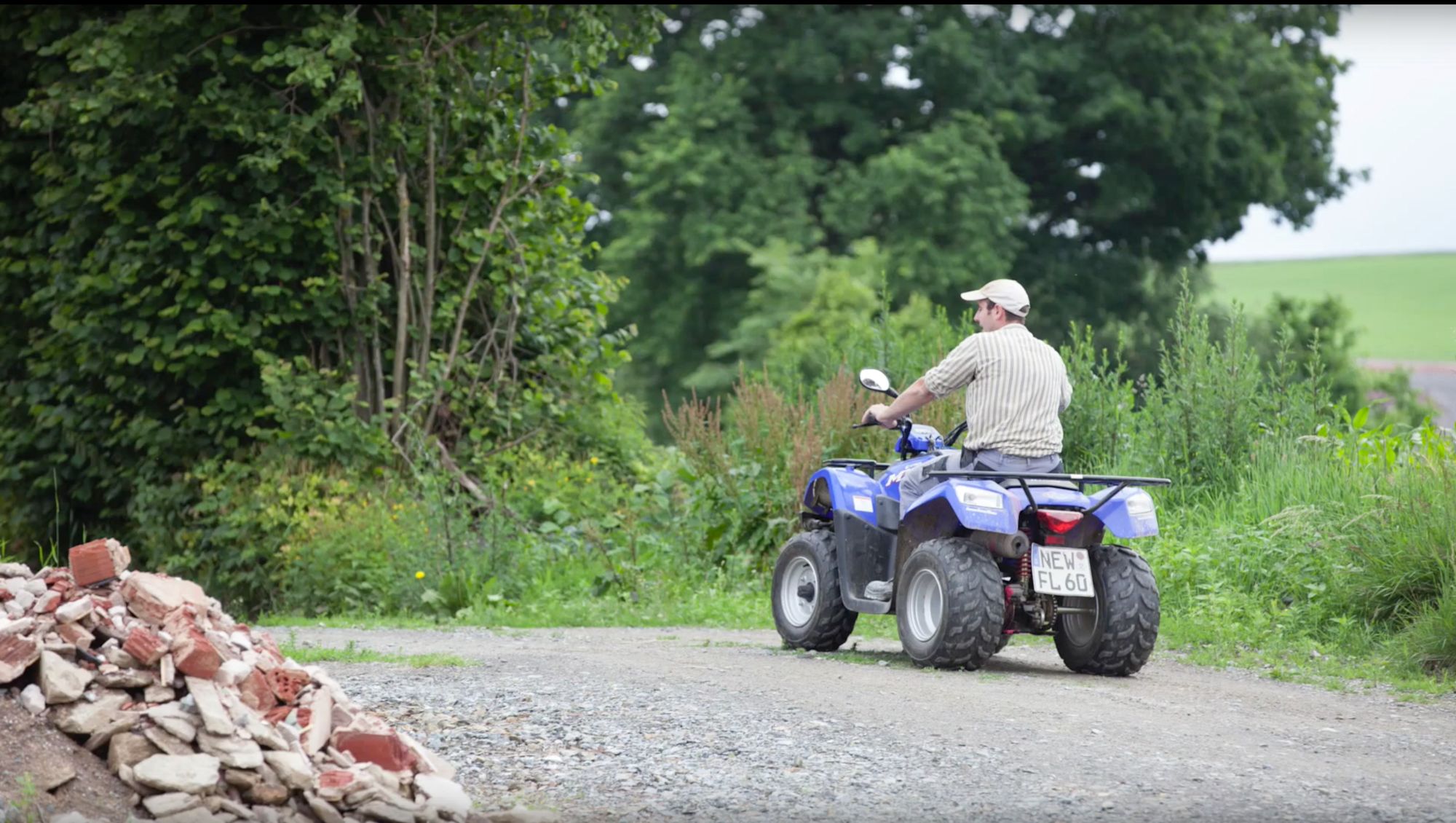 Mann fährt mit einem Quad über einen Schotterweg an einem Schutthaufen vorbei