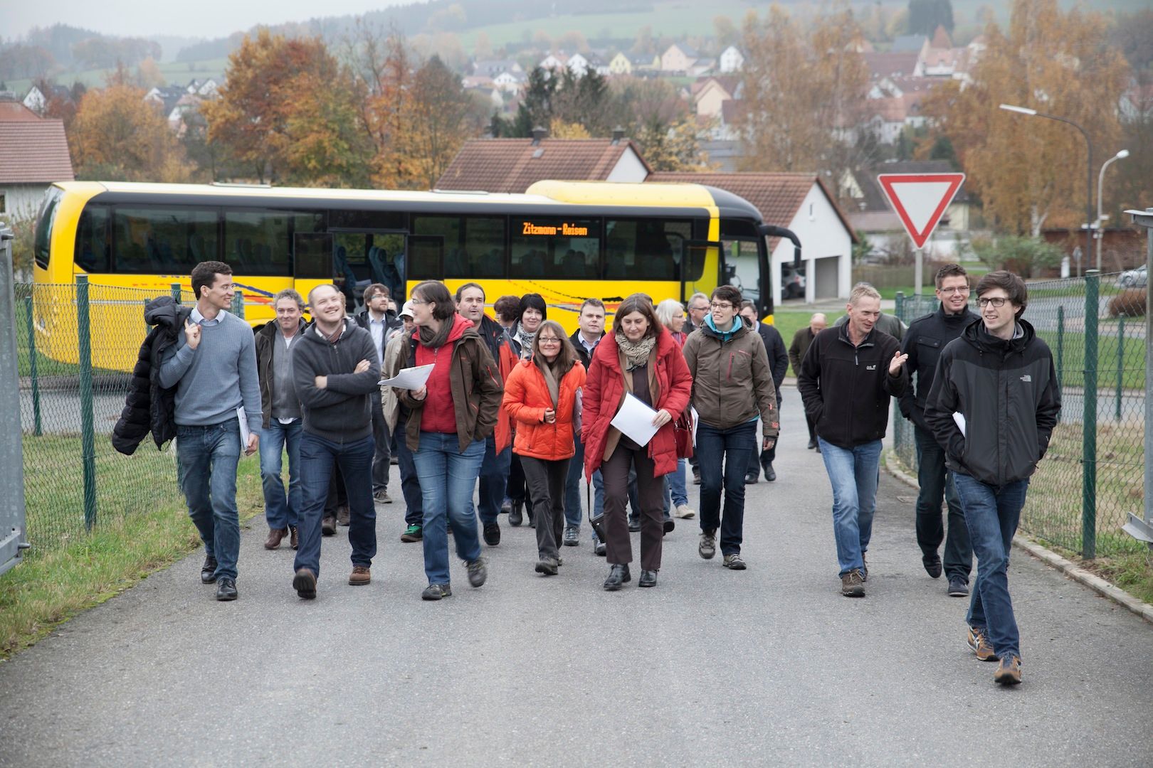 Gruppe von Menschen läuft im Herbst an einem gelben Reisebus entlang