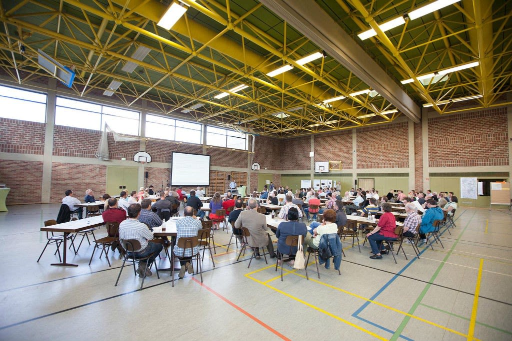 Zahlreiche Menschen sitzen in einer Sporthalle bei einer Informationsveranstaltung