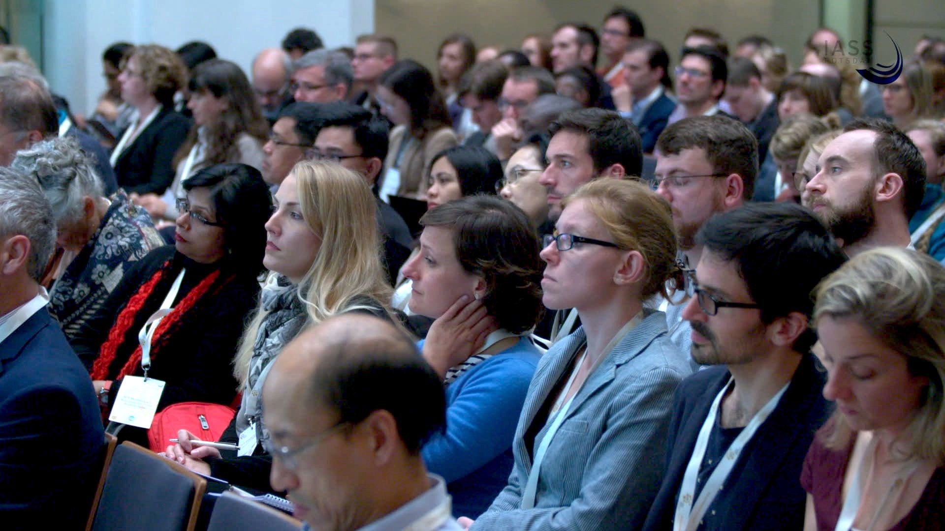 Aufmerksames Konferenzpublikum sitzt in dichten Stuhlreihen
