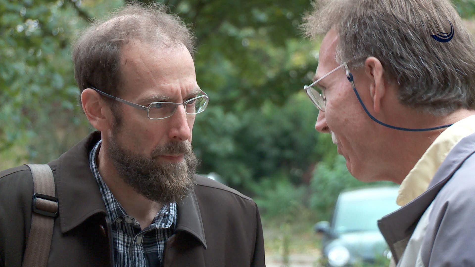 Zwei bärtige Männer diskutieren im Freien vor Grün
