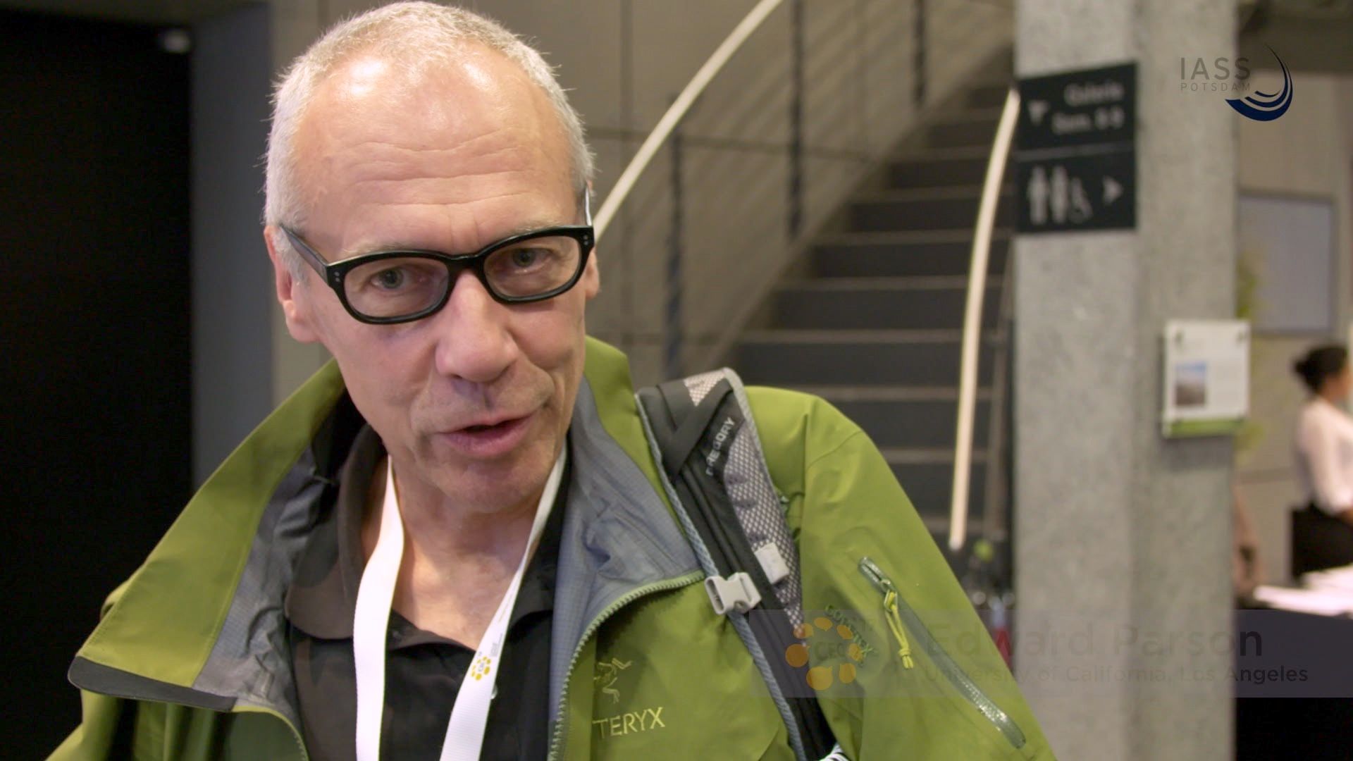 Mann mit grüner Jacke und Rucksack im Interview vor einer Treppe