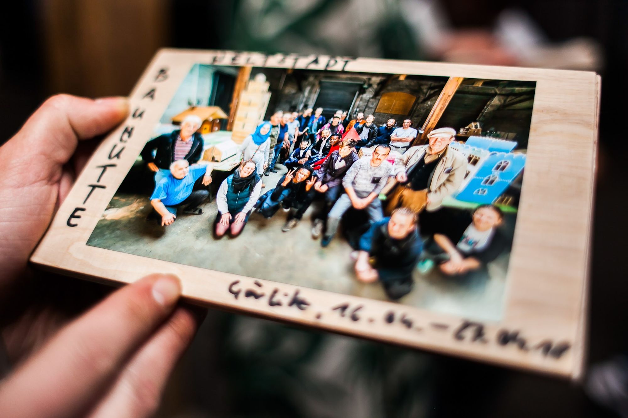 Hand hält Rahmen mit Gruppenfoto der Werkstattteilnehmenden, beschriftet „Baumhütte“