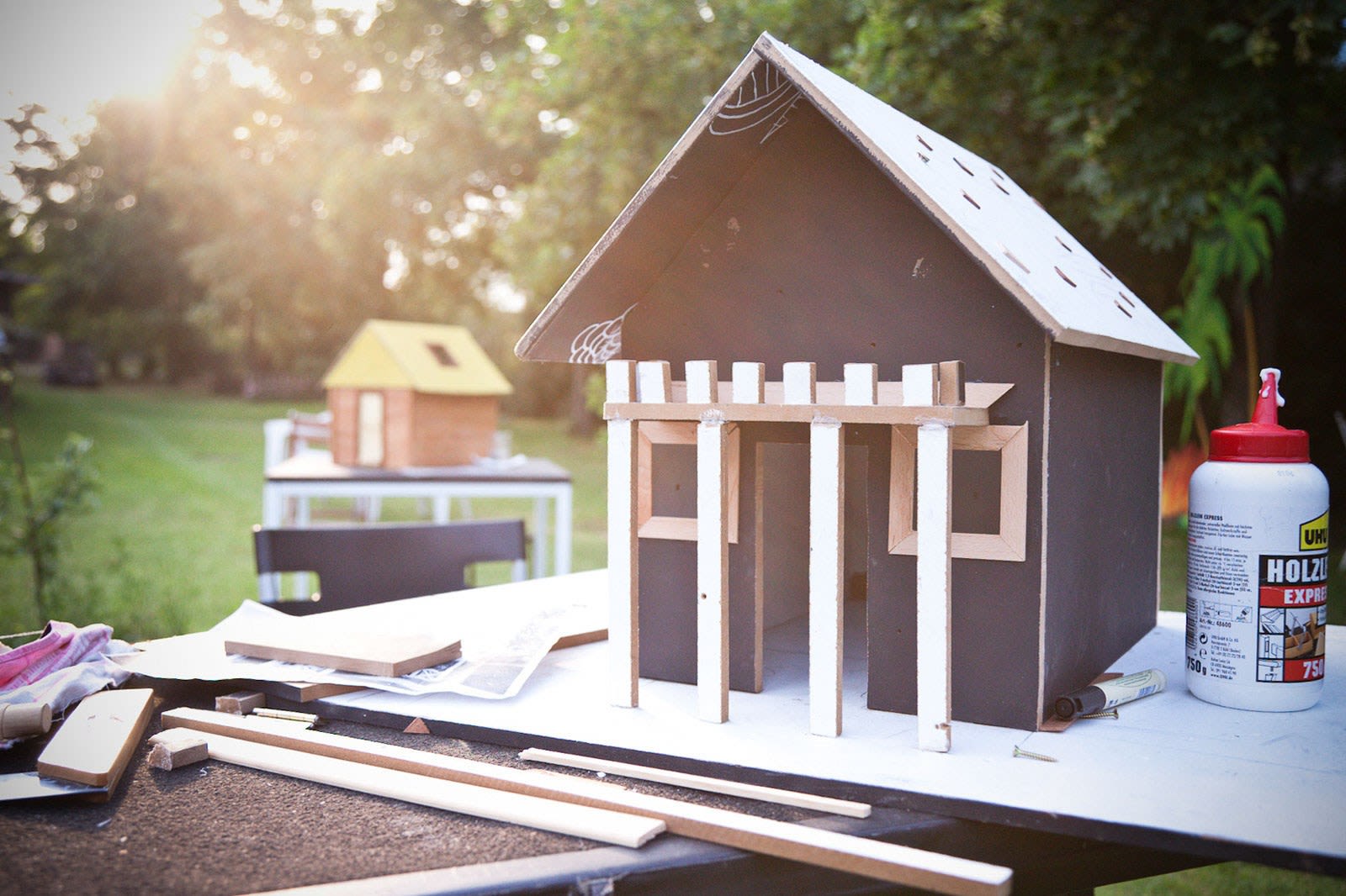 Hölzernes Hausmodell mit weißer Veranda auf Gartentisch im Abendlicht
