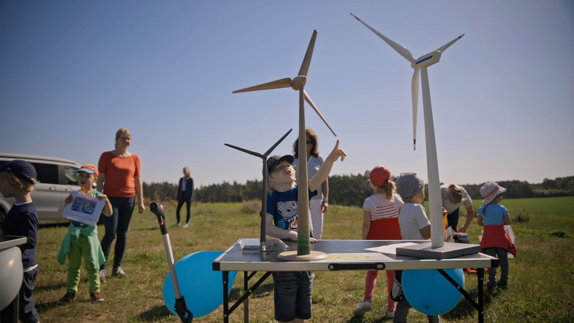 Kinder bestaunen im Freien kleine Windradmodelle auf einem Klapptisch