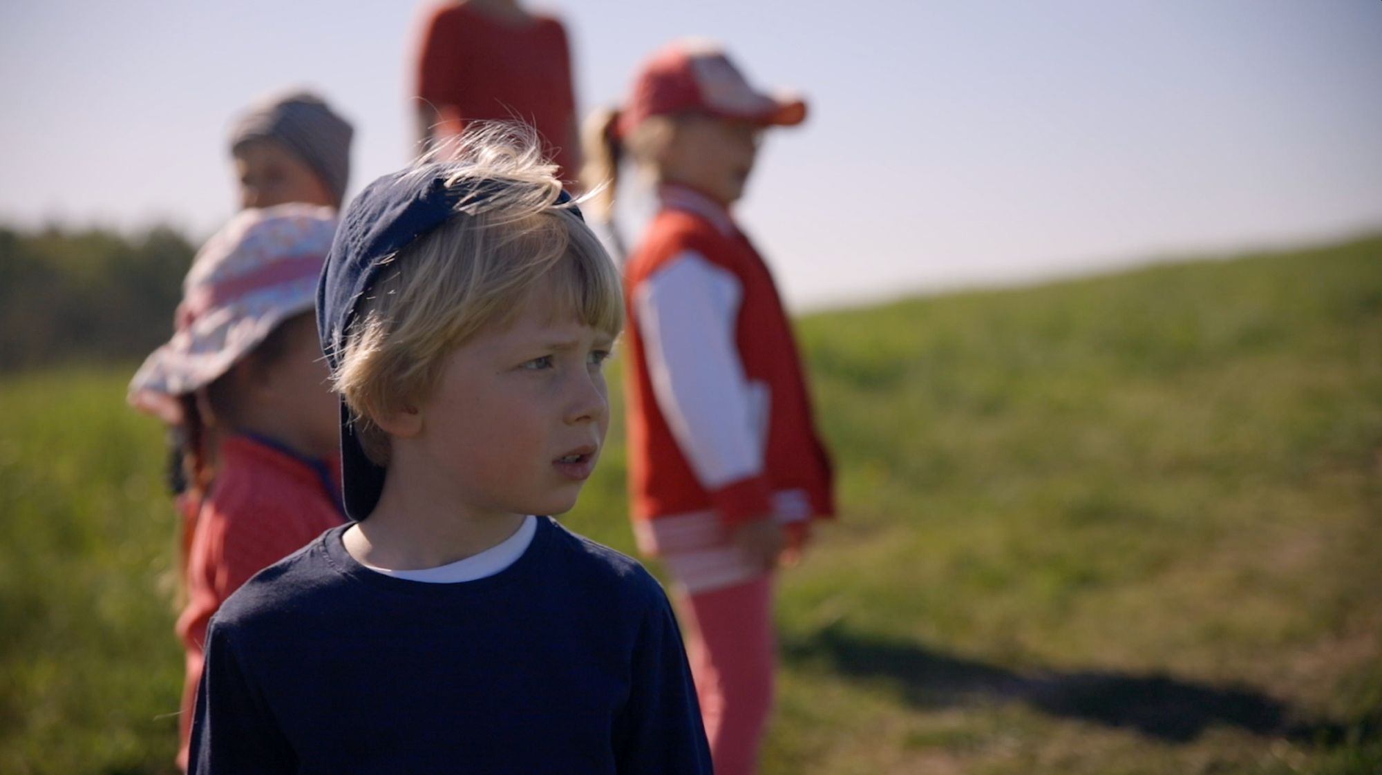Junge im Feld blickt zur Seite, im Hintergrund weitere Kinder in Rot