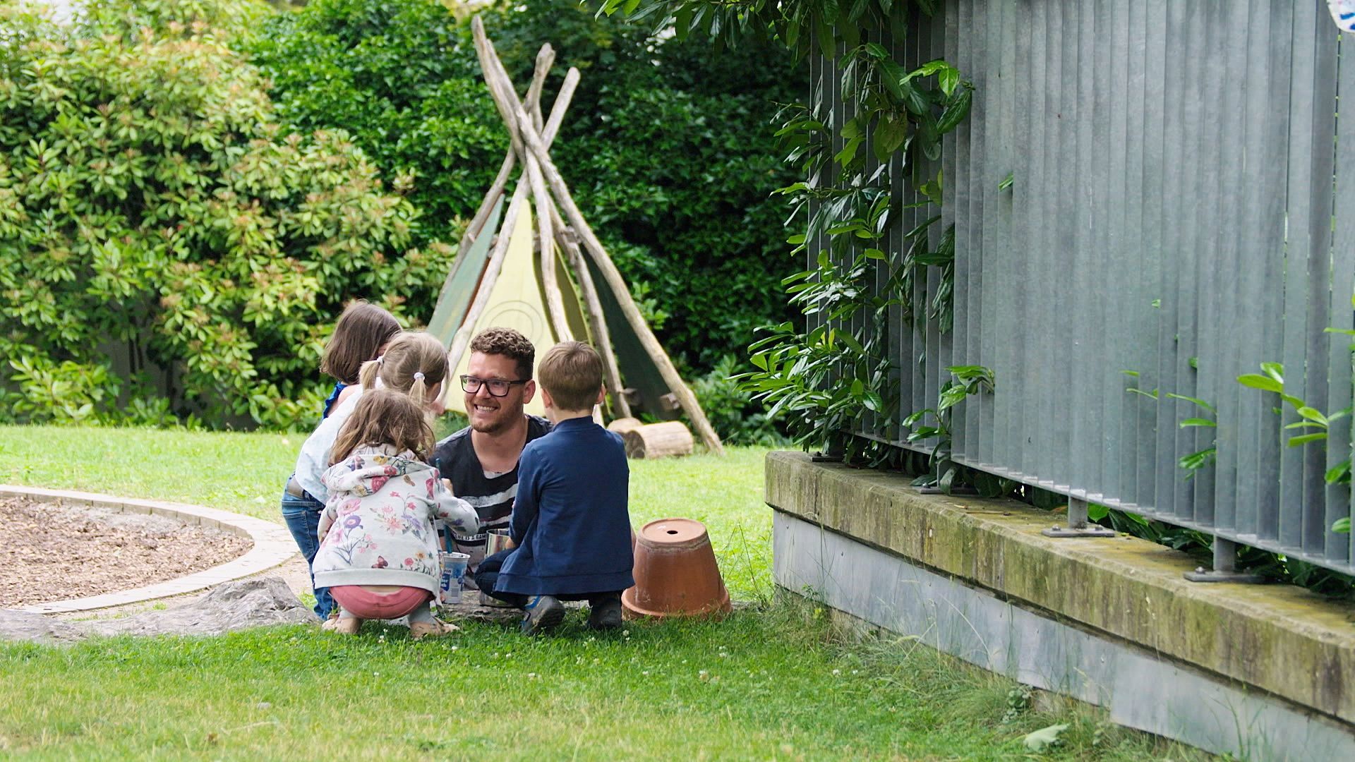 Ein Betreuer sitzt mit mehreren Kindern im Garten vor einem Tipi