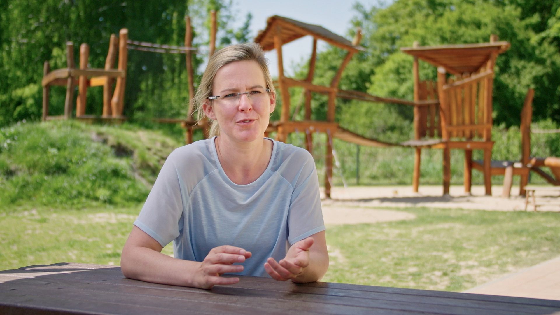 Frau im Interview vor einem hölzernen Spielplatz im Freien