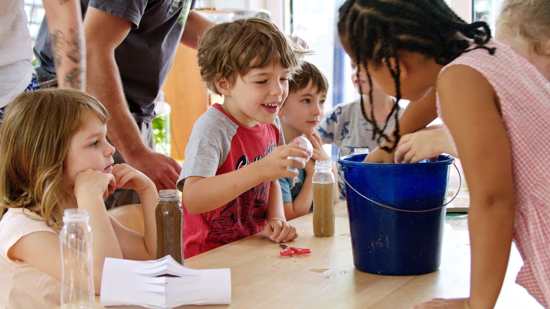 Kinder untersuchen an einem Tisch Wasserproben in Flaschen und einem Eimer