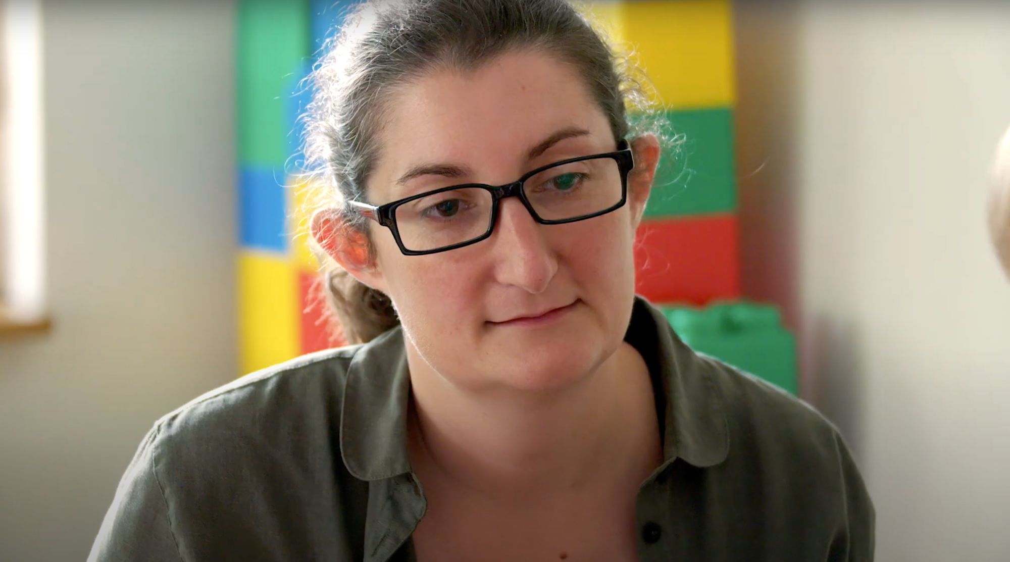 Frau mit Brille im Gespräch, im Hintergrund bunte Bauklötze
