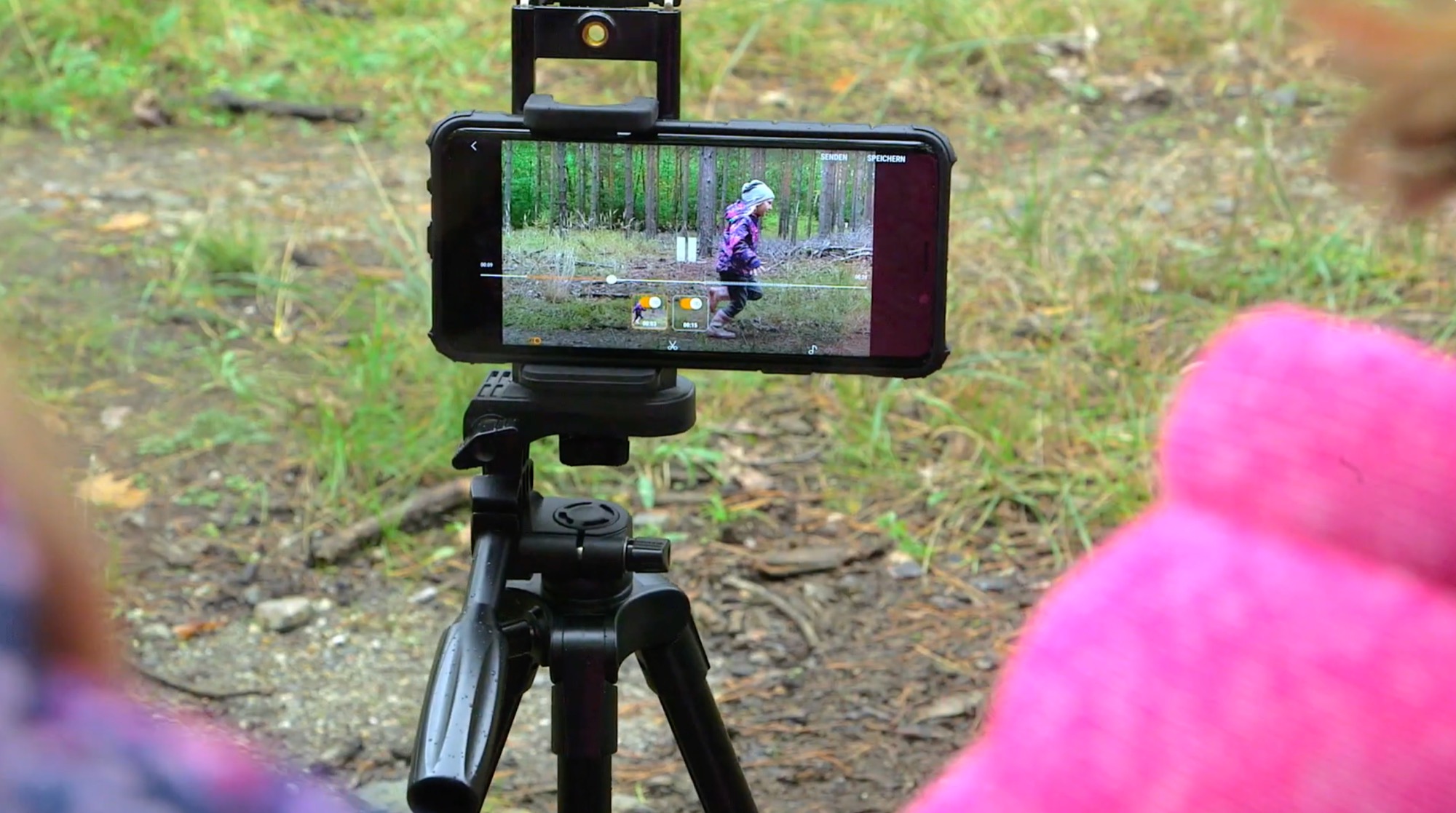 Smartphone auf einem Stativ filmt ein Kind, das im Wald läuft
