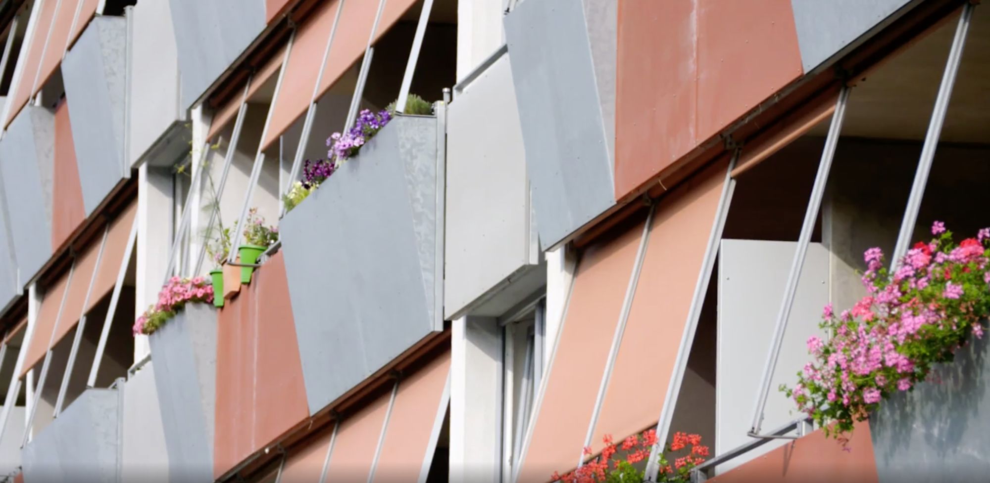 Fassade mit ausgefahrenen Sonnenmarkisen und blühenden Blumenkästen an Balkonen