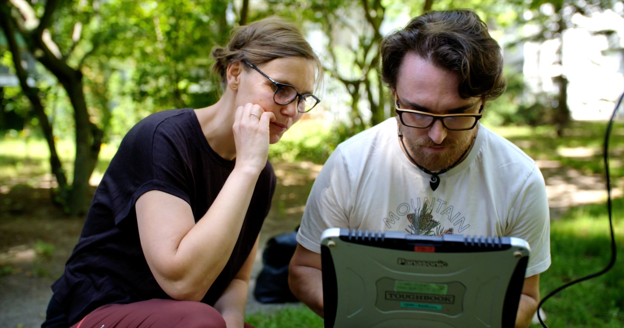 Zwei Personen betrachten im Grünen ein robustes Outdoor-Laptop