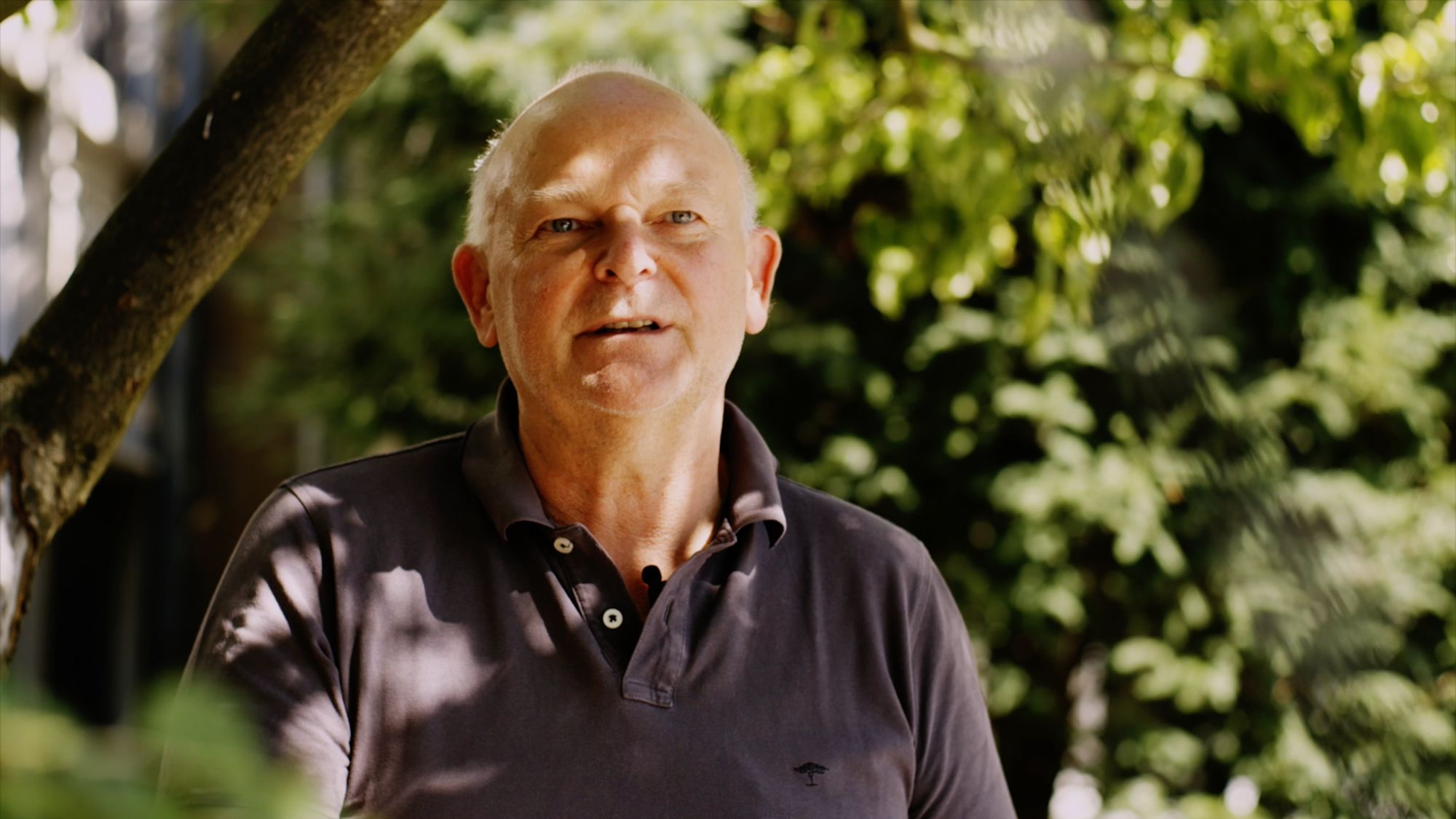 Ein älterer Mann im Poloshirt spricht im Freien vor grünem Hintergrund