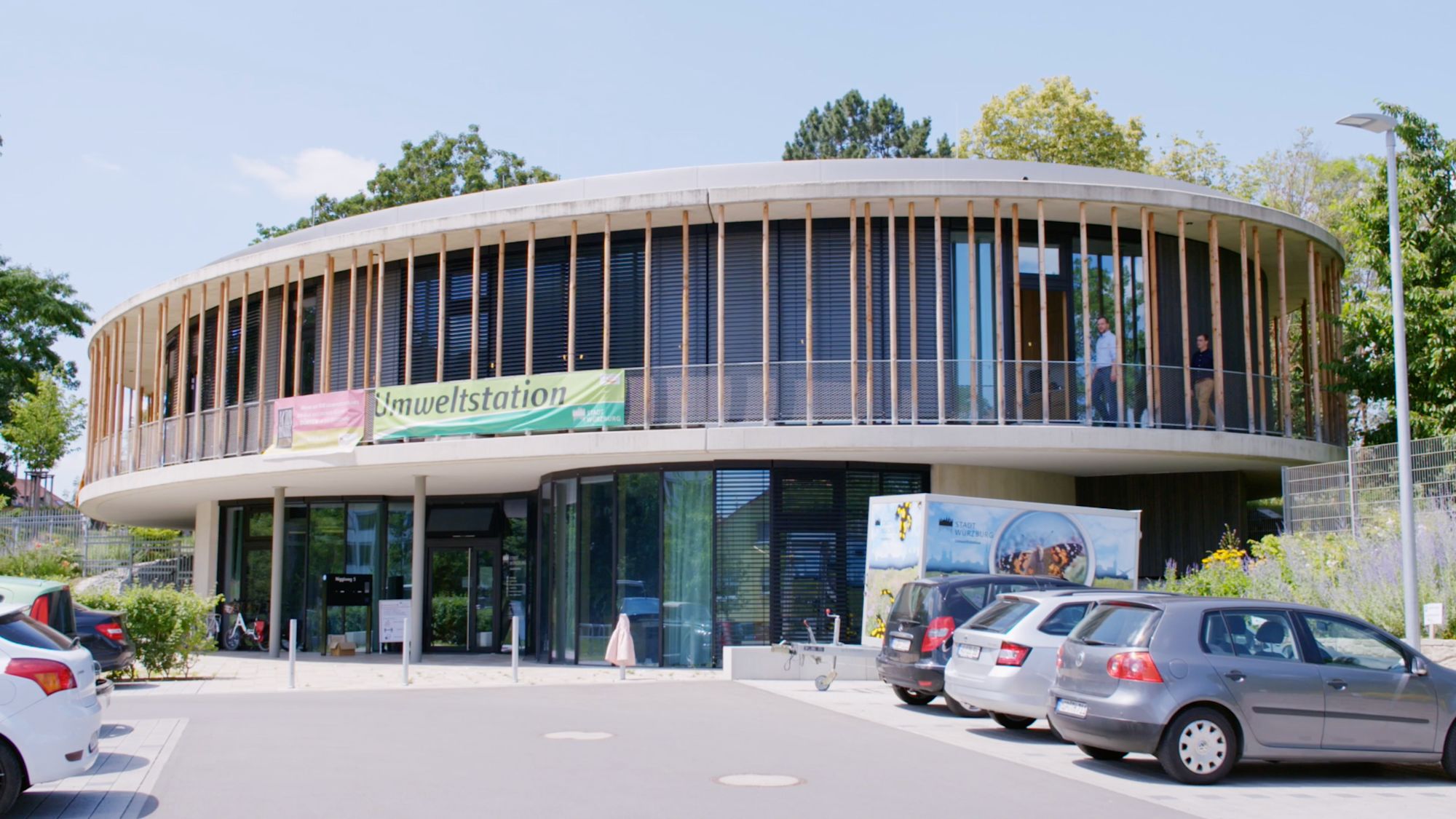 Runder Neubau der Umweltstation mit Banner und parkenden Autos davor