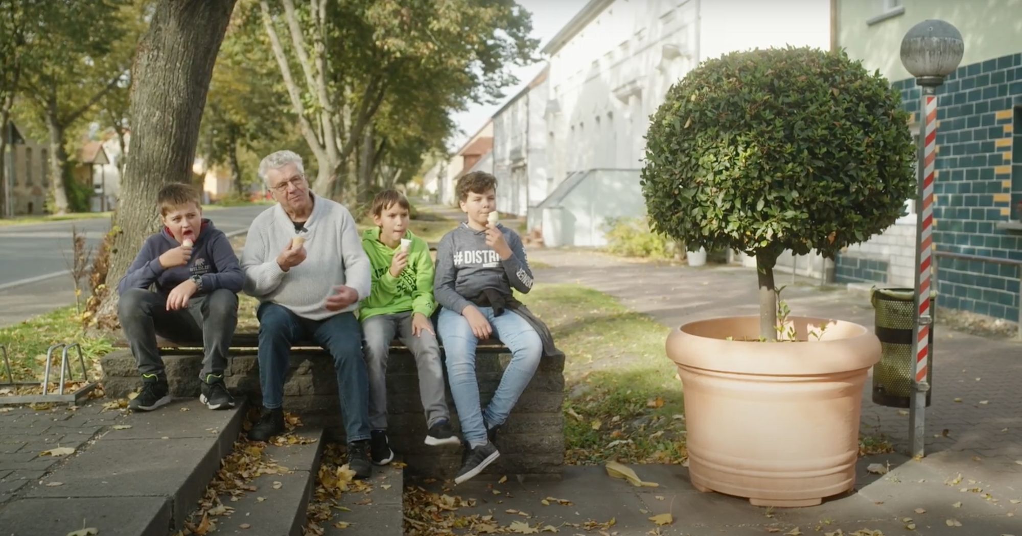 Drei Jungen und ein älterer Mann essen Eis auf einer Mauer in der Dorfstraße