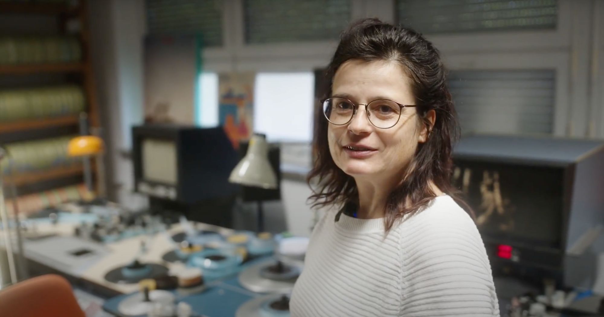 Eine Frau mit Brille steht in einem Archivraum mit alten Filmspulengeräten