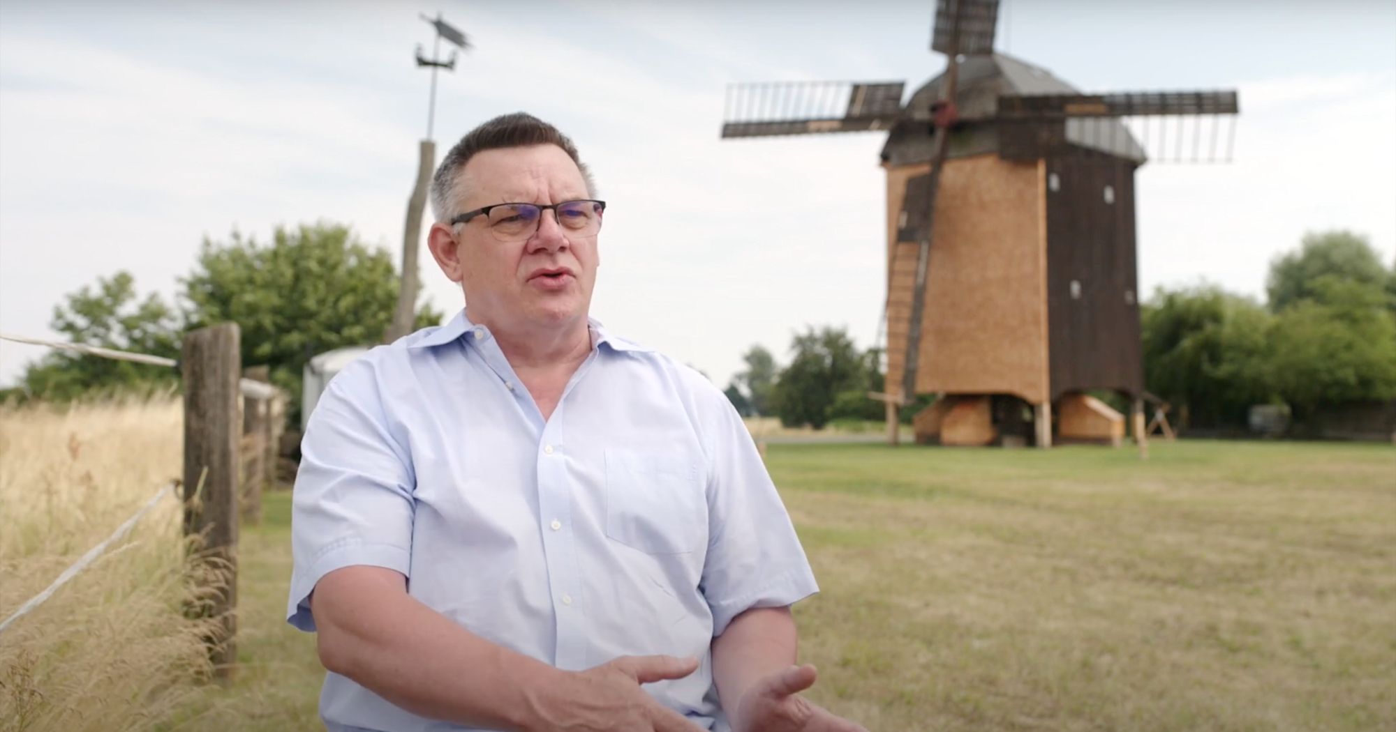 Mann mit Brille spricht im Freien, im Hintergrund die restaurierte Bockwindmühle