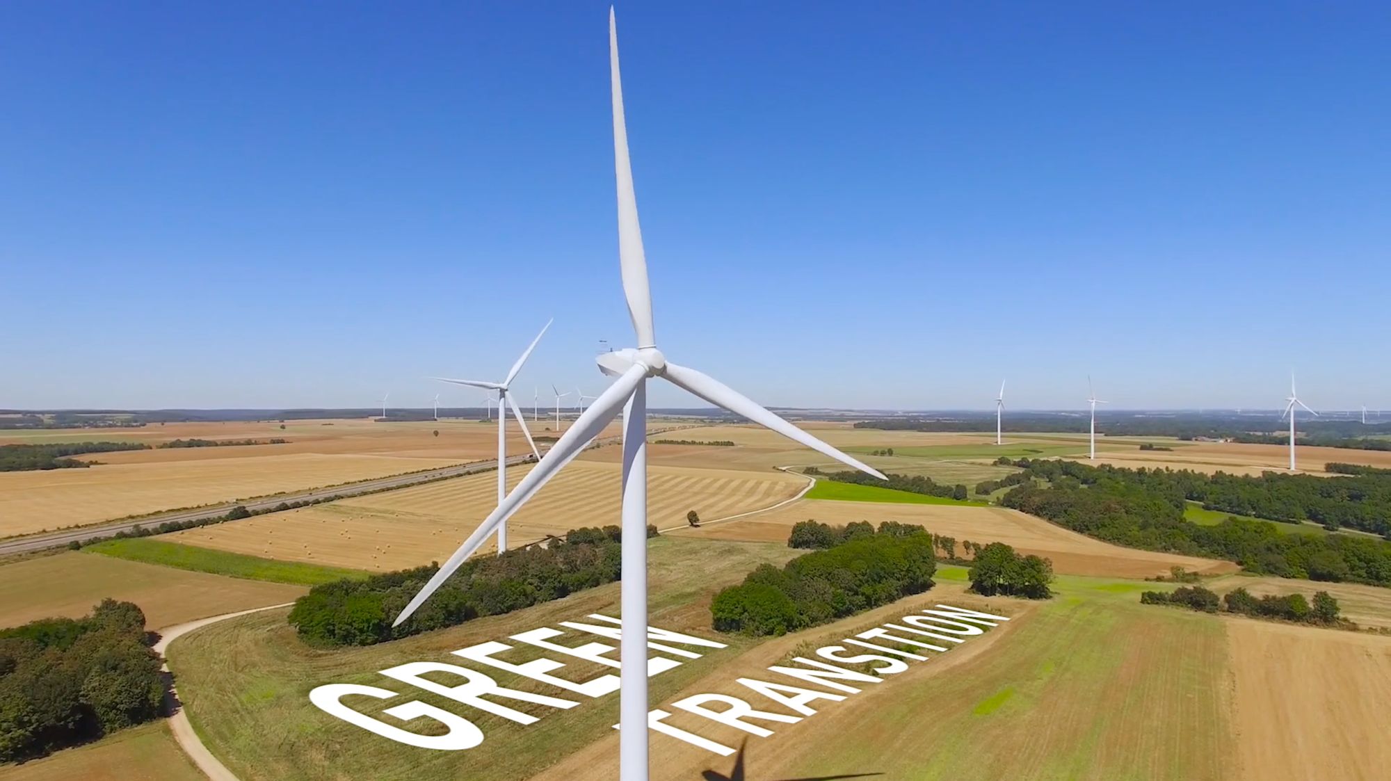Windkraftanlagen in Feldlandschaft mit Schriftzug „Green Transition“