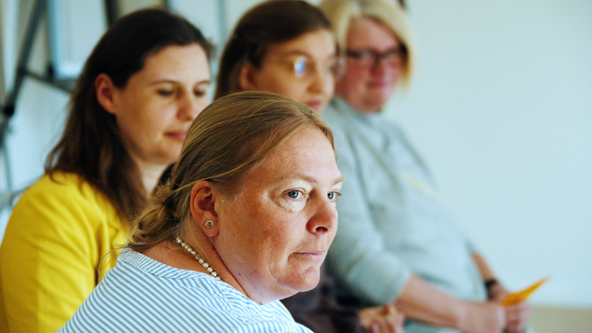 Frau im Profil, im unscharfen Hintergrund weitere sitzende Teilnehmende