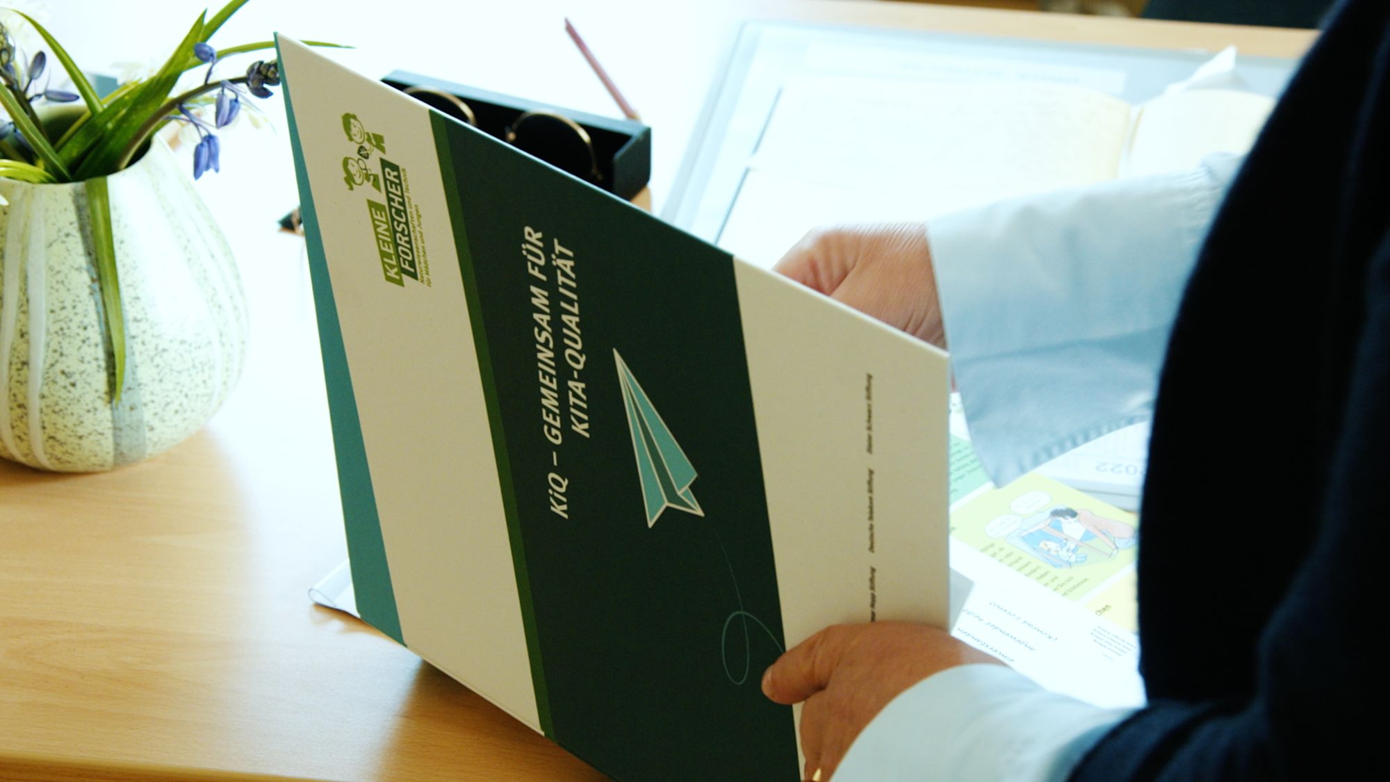 Hand hält eine Broschüre mit dem Titel „KiQ – Gemeinsam für Kita-Qualität“