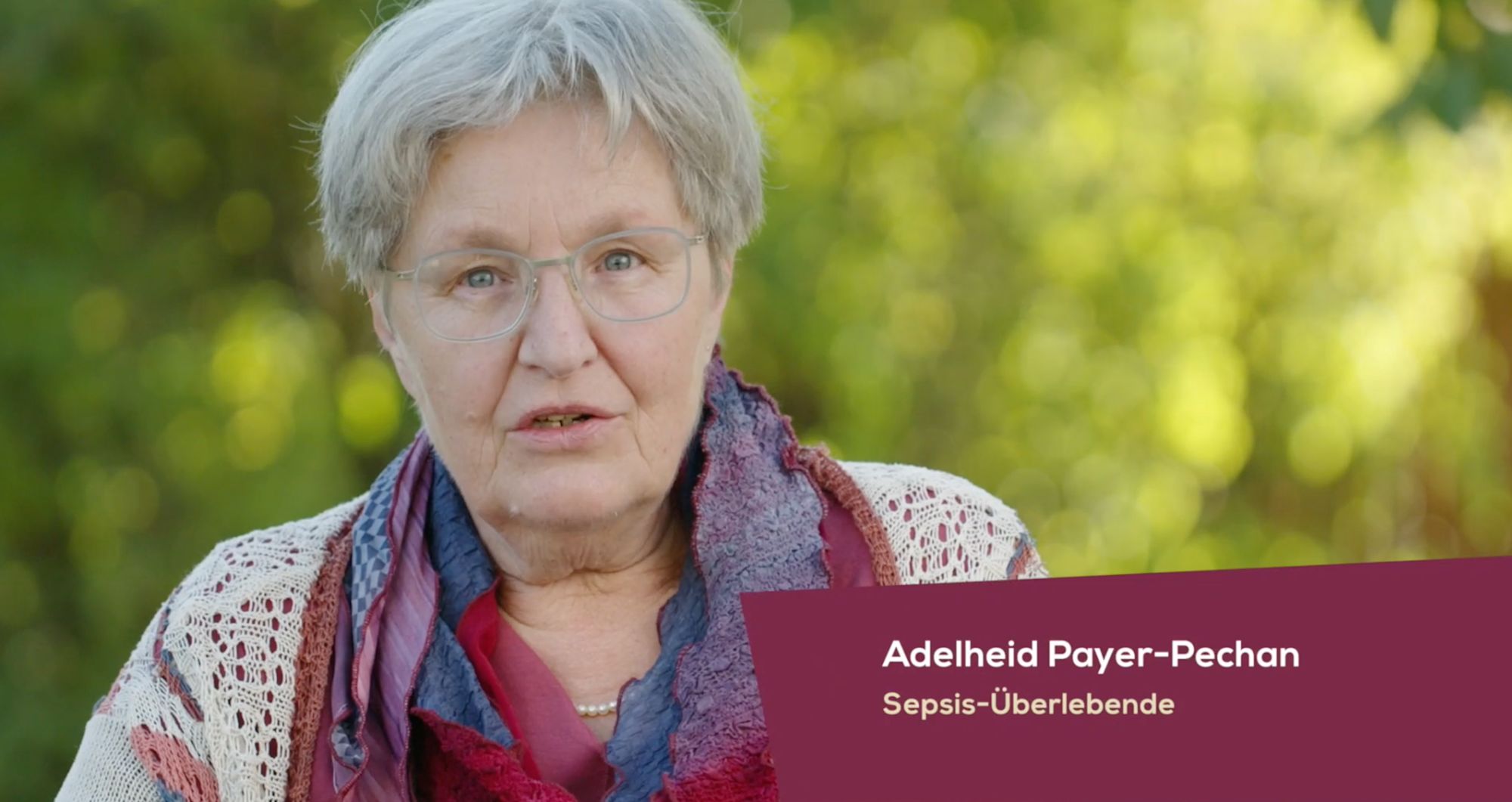 Ältere Frau mit buntem Schal im Freien, Einblendung „Adelheid Payer-Pechan“