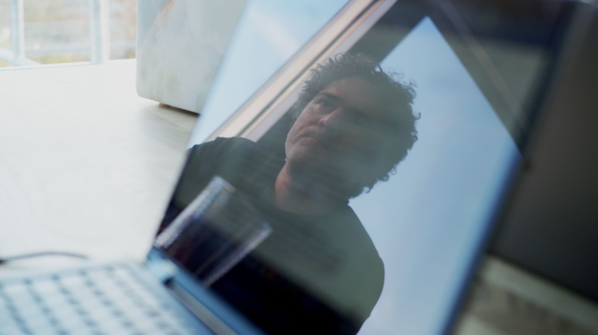 Im Laptop-Bildschirm gespiegeltes Porträt eines Mannes mit lockigem Haar