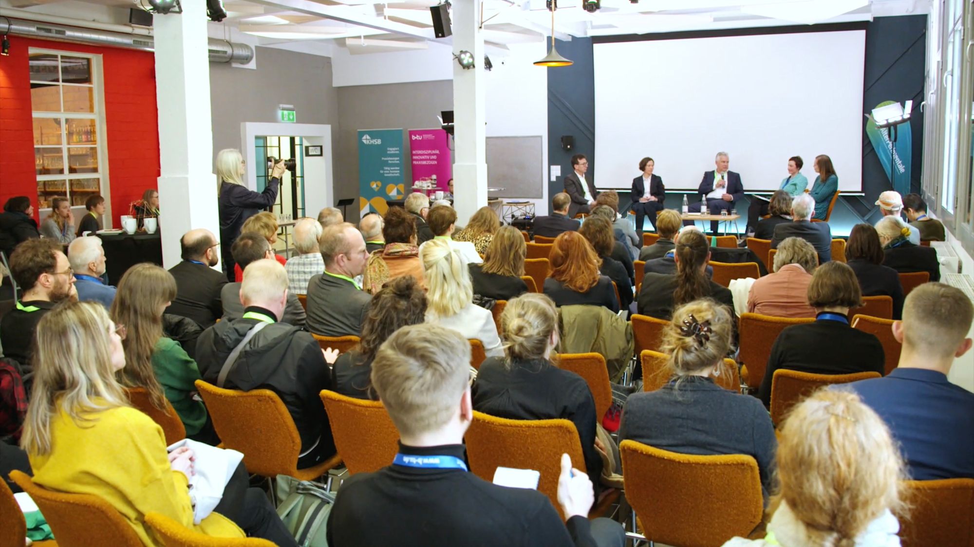 Podiumsdiskussion vor großem Publikum in einem Veranstaltungssaal
