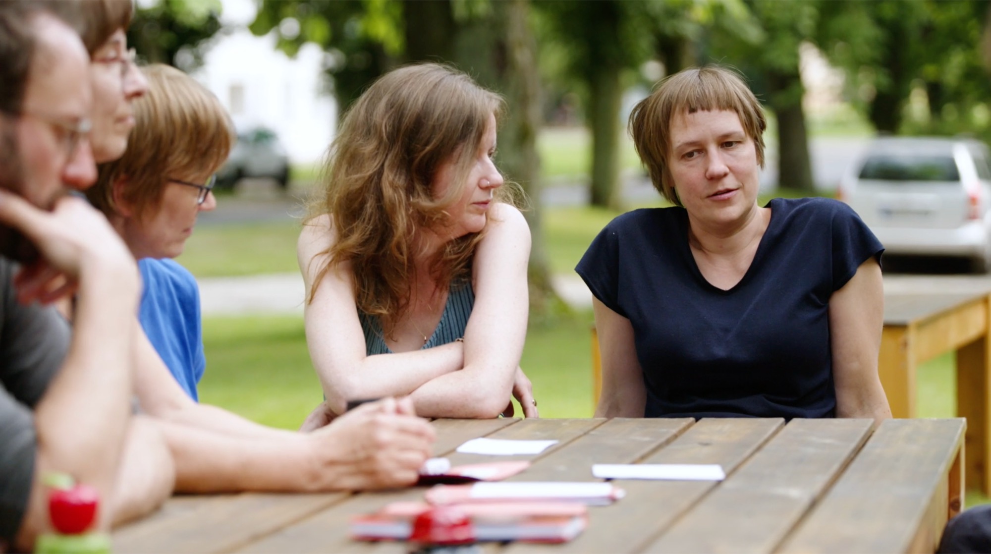 Zwei Frauen im Gespräch an einem Tisch im Freien, im Hintergrund weitere Teilnehmende