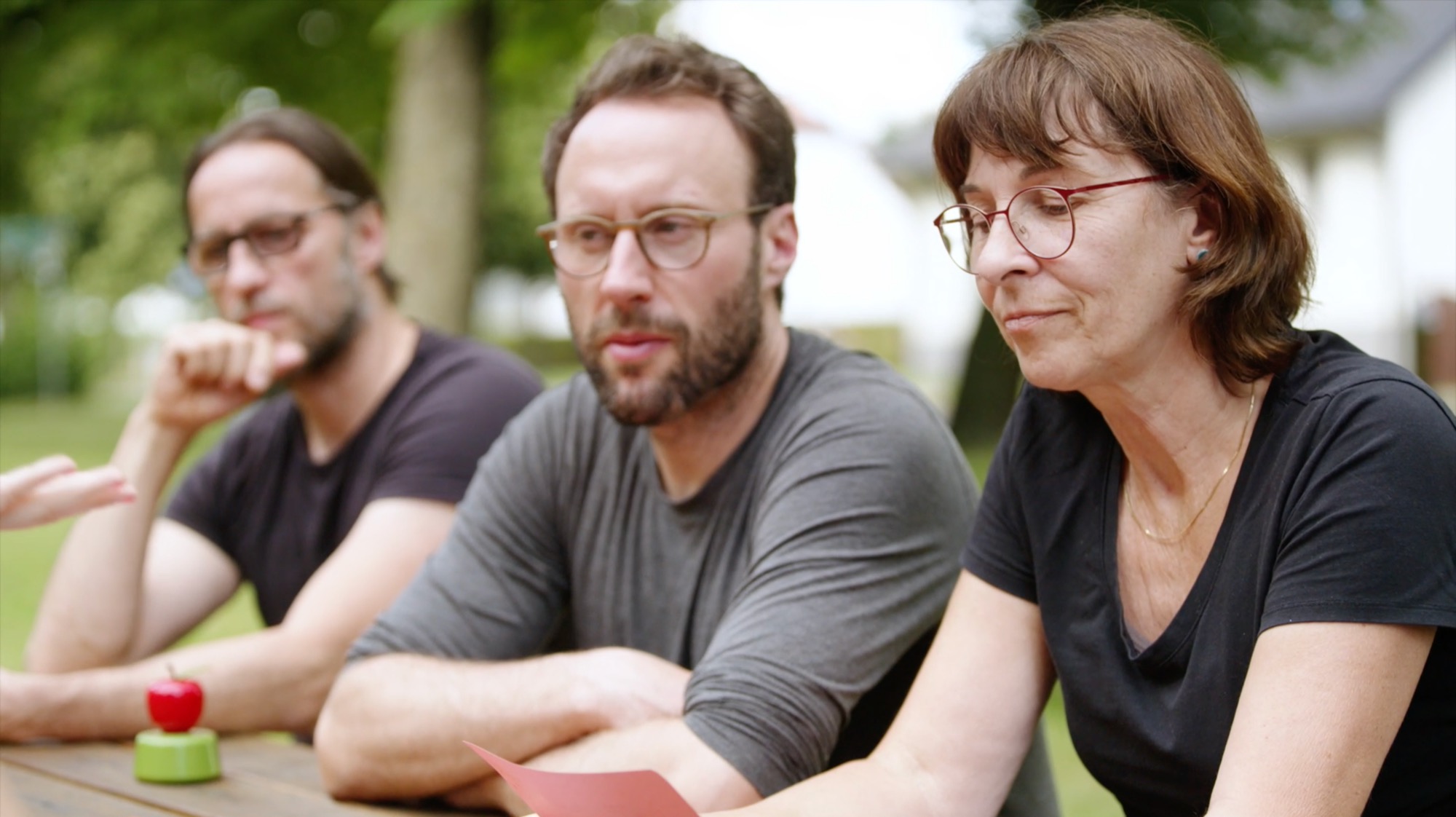 Drei Personen sitzen im Gespräch nebeneinander an einem Tisch im Freien