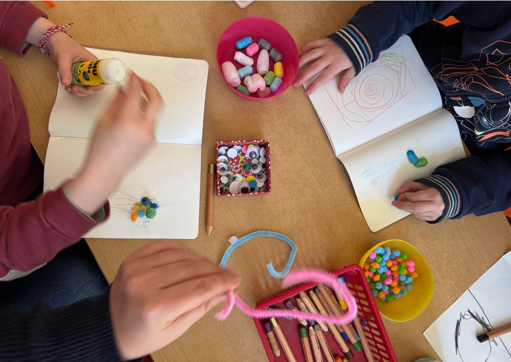 Kinder basteln am Tisch bunte Mikroben-Figuren aus Wackelaugen und Pfeifenreinigern