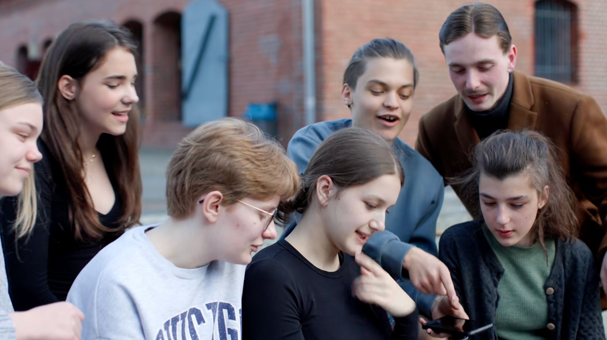 Gruppe Jugendlicher blickt lachend gemeinsam auf ein Smartphone im Freien