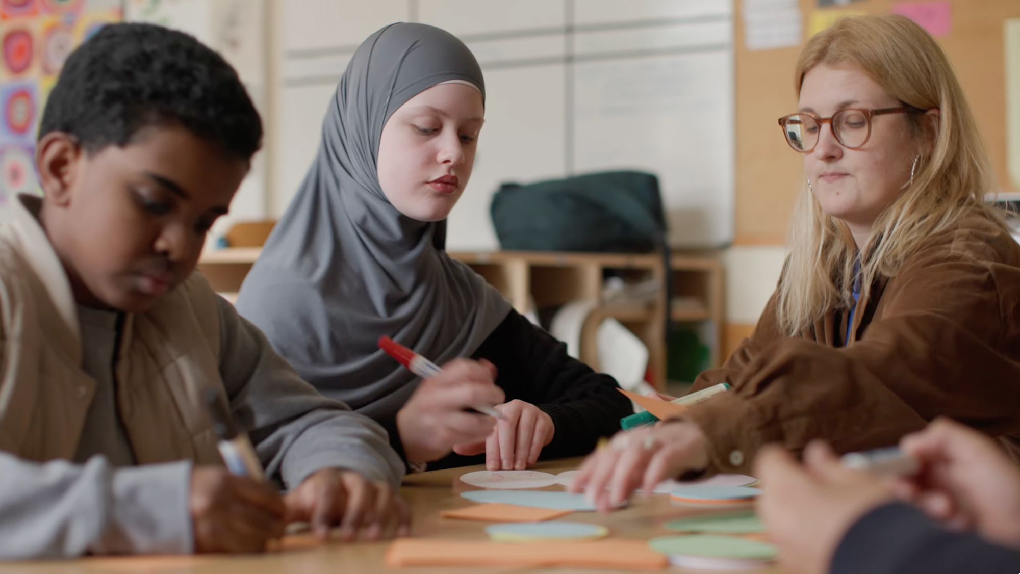 Kinder und eine Frau gestalten gemeinsam bunte Papierformen an einem Tisch