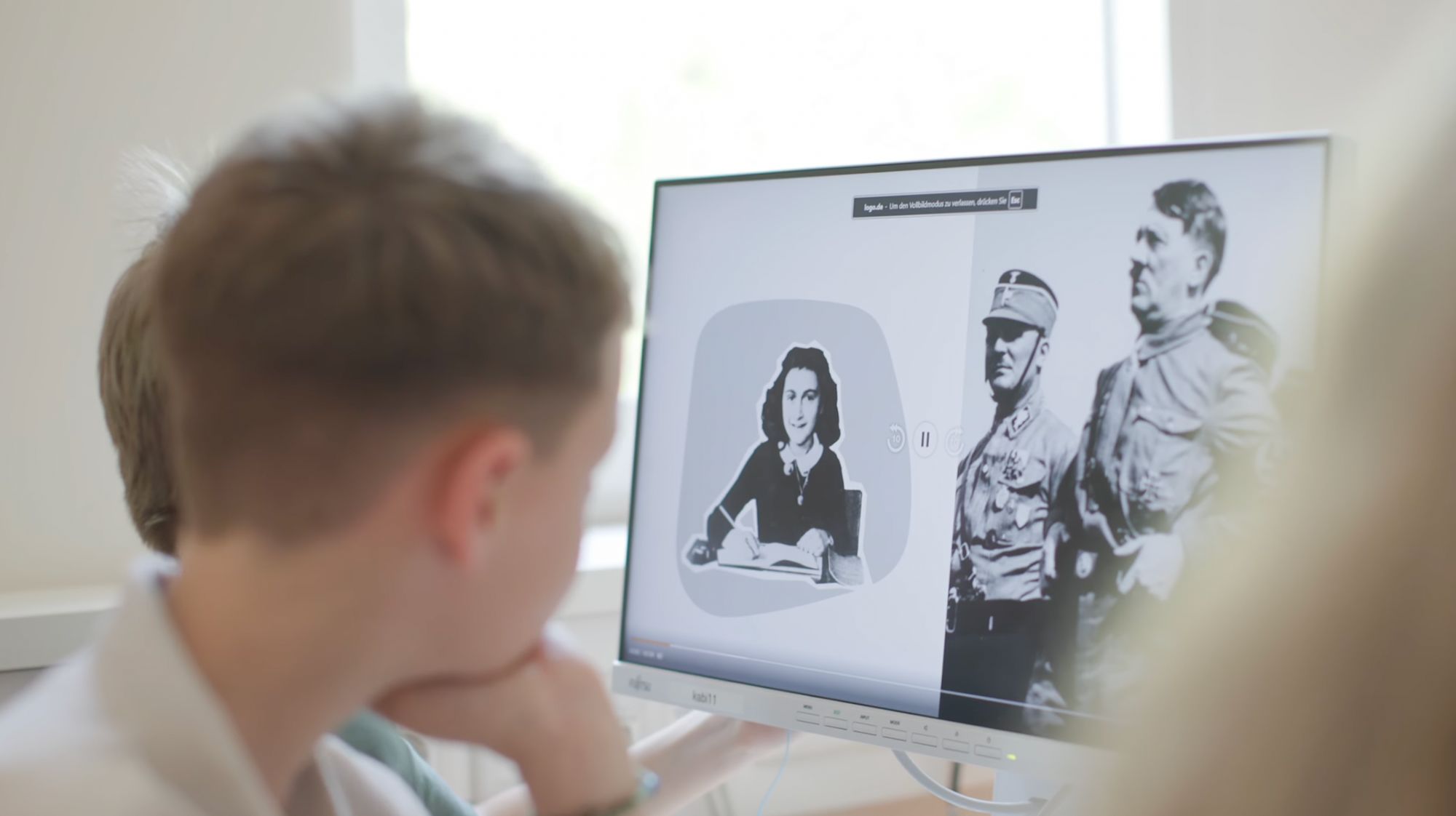 Junge betrachtet einen Bildschirm mit einer Illustration und historischen Kriegsfotos