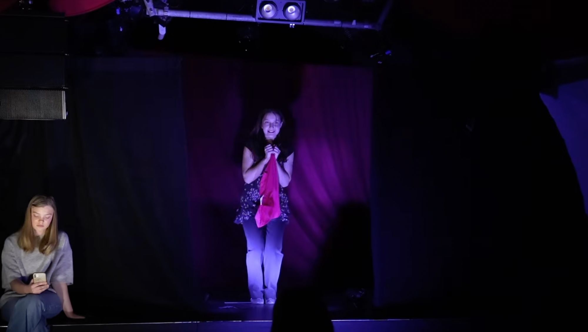 Mädchen singt auf einer Bühne im violetten Scheinwerferlicht mit rosa Tuch in den Händen